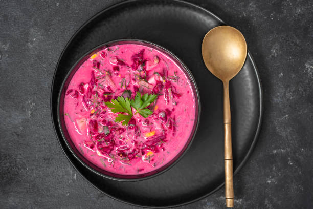 Delicious cold summer beetroot soup with cucumber, boiled egg, radish in black bowl on table, close up, top view